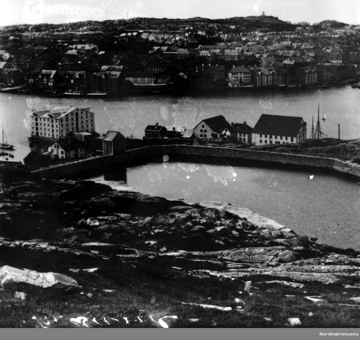 Fra Innlandet, fotografert fra Bautaen, hvor vi ser vannreservoaret i front. Brygger. På andre siden av havnebassenget finner vi Kirkelandet. Fra Nordmøre Museums fotosamlinger.
