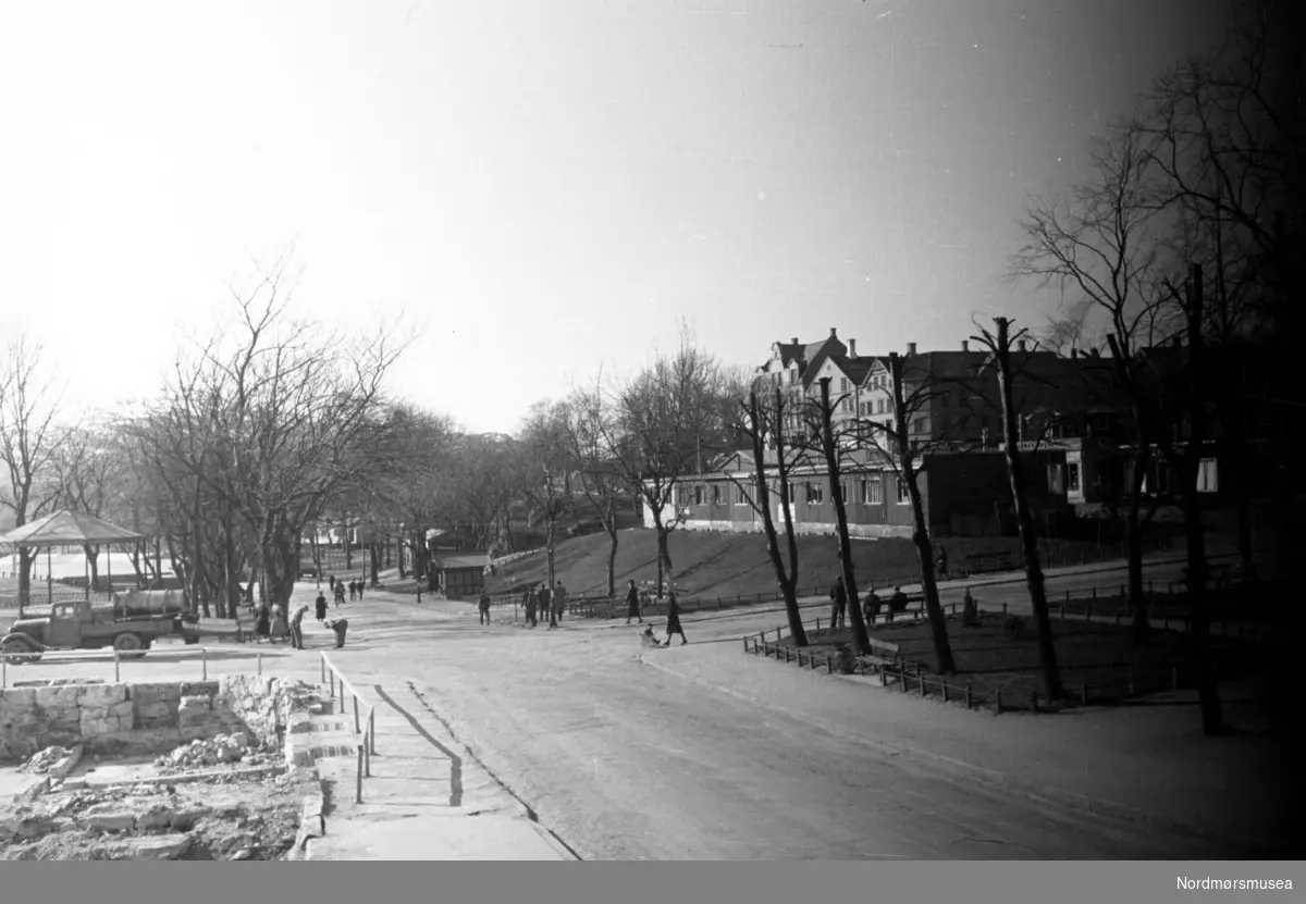 ";Gjenreisningsbyen"; Kristiansund. Her ser vi fra krysset Langveien/Skolegata på Kirkelandet i Kristiansund, med litt av musikkpaviljongen i bakgrunnen til venstre, samt
flere brakker på høyre side - på Kirketomta. Barmanhaugen bak. Fastinggårdens murer til venstre. Øverparken. . Bildet kan trolig dateres til okkupasjonsårene 1940 til 1945. Fra Nordmøre Museums fotosamlinger.
