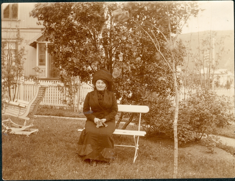 Portrett. Fru Rasmus Dahl, som enke, sitter på en hagebenk.