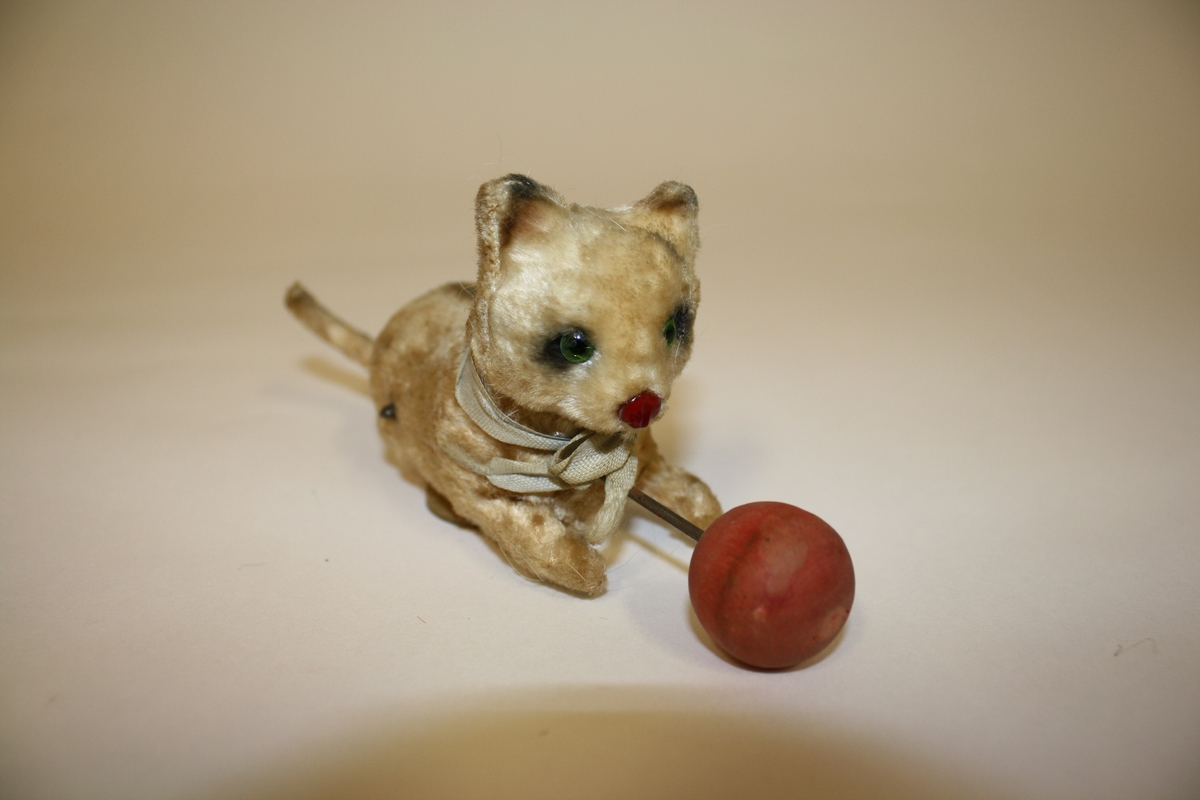 Gitt av Lisbeth Andreassen Chumak. Liten katt med ball og sløyfebånd. Ballen er festet til katten med stålstreng. Fra 1950 tallet.