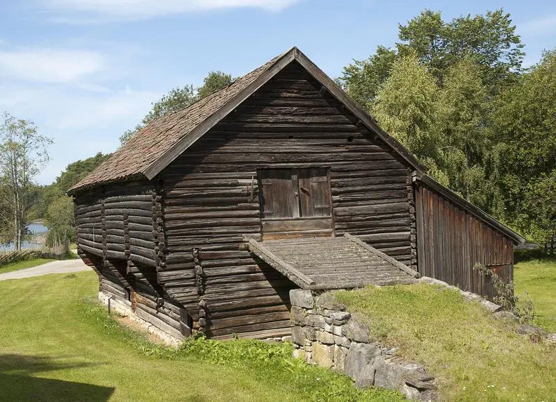 Stor tømmerstall med utbygd andreetasje og låvebru opp til låvedør i gavlveggen.