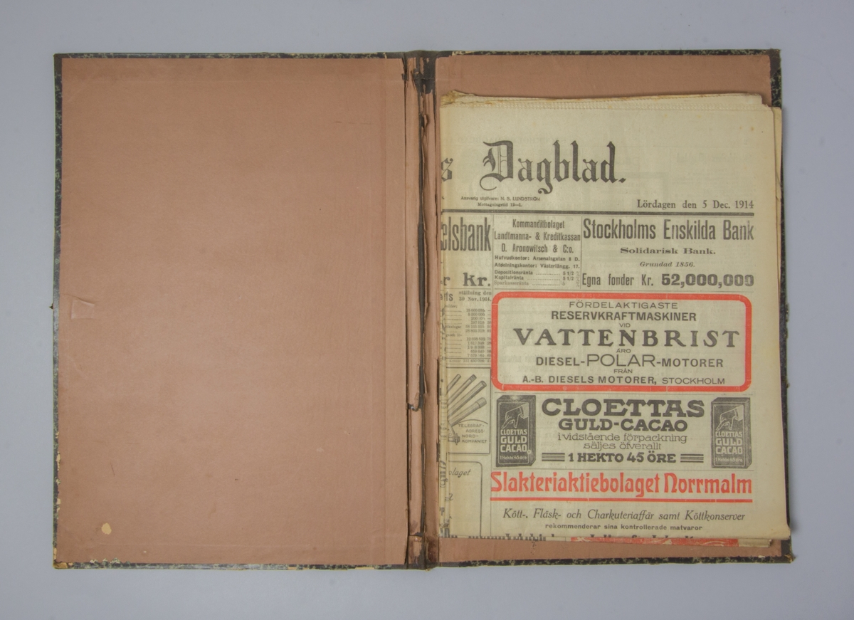 Portfölj av marmorerad papp. Sammanhållen med knytband. Rygg av svart linne. Innehåller enbart flera exemplar av Stockholms Dagblad från 1914.