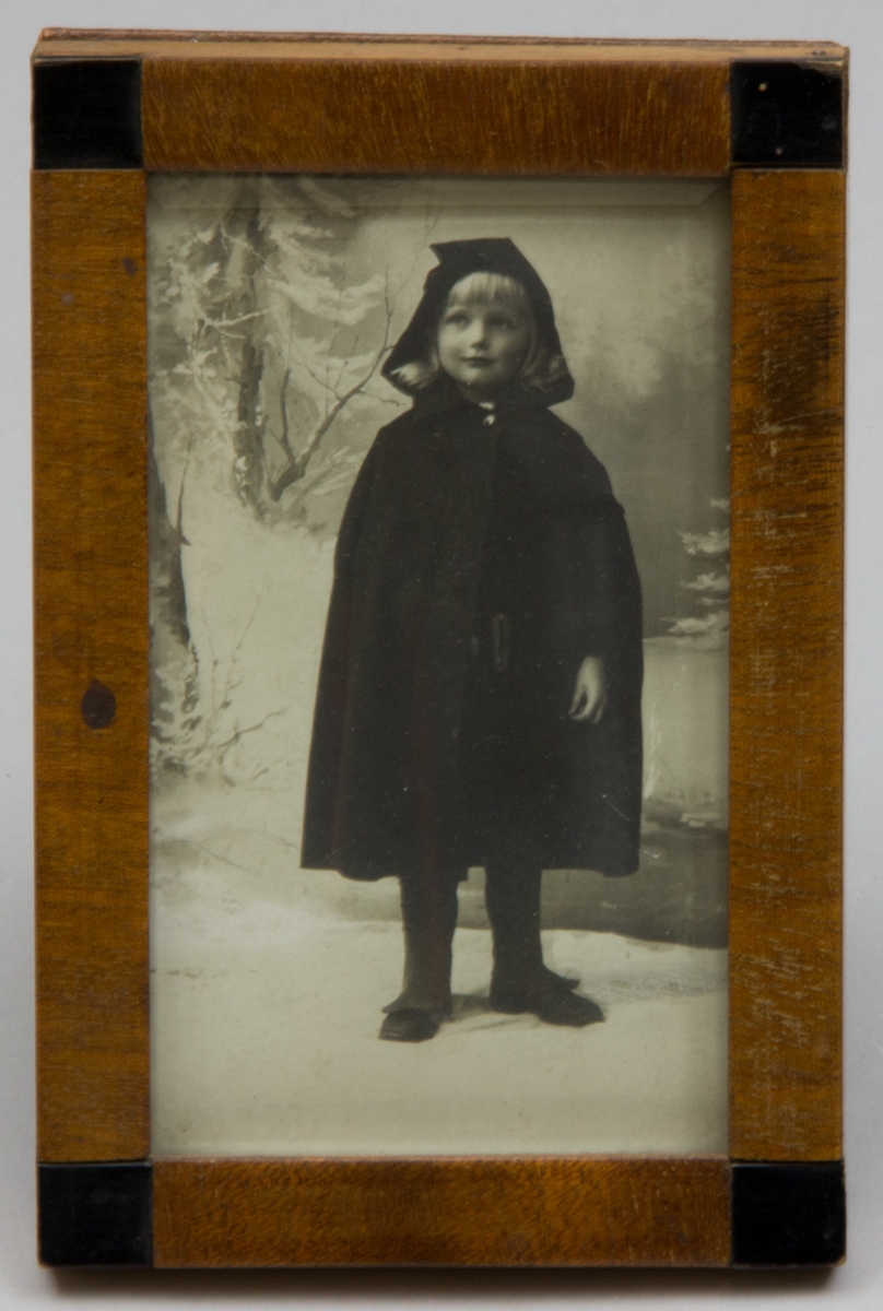 Porträttfotografi föreställande Staffan Kronberg som ung, uppskattningsvis 4 år, i knälång capé med huva i vinterlandskap, ateljébild.