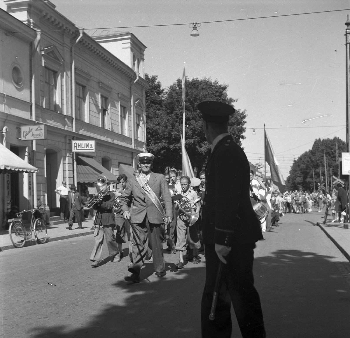 Gävleutställningen 1946 vid Gävletravet. Med flaggor i täten tågar gossorkestern med sin ledare J. Haglund till utställningen genom stan