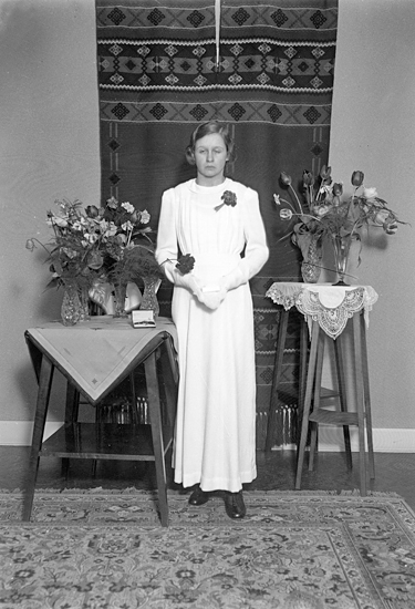 Foto av en okänd kvinnlig konfirmand i lång vit konfirmationsklänning.