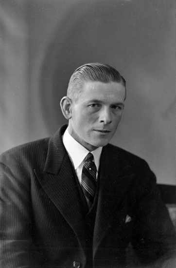 Foto av en man i mörk kostym och randig slips med kråsnål.
Midjebild, halvprofil. Ateljéfoto.
Kan ev. vara: Johan Einar Uno Bengtsson (1895-1968), Hjortsberga.
Källa: Sveriges Dödbok 1901-2009.