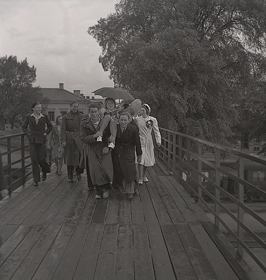 Studenterna 1940. 31/5 - 1/6. En kvinnlig student bärs längs med gångbron över järnvägen, från Norra Järnvägsgatan.