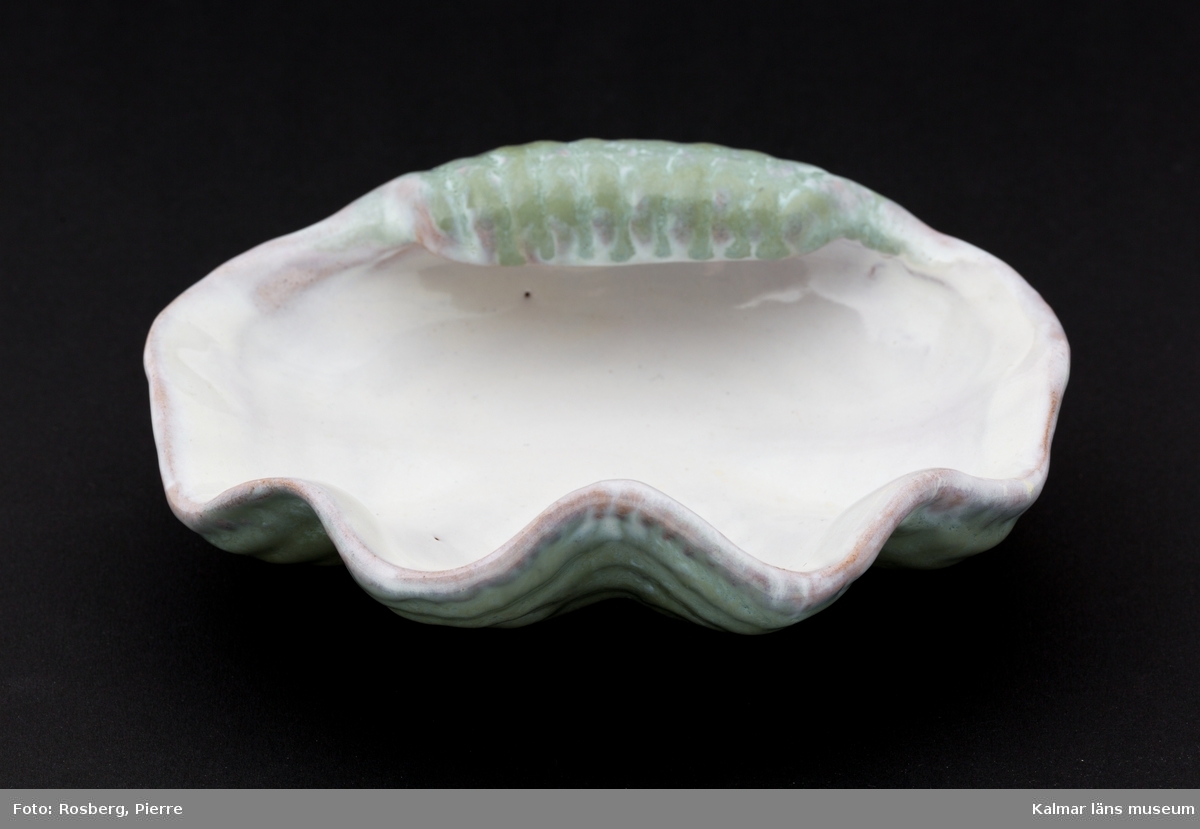 KLM 45058:44. Askfat, av keramik. Askkopp av glaserad keramik i ljust grönt och rosatonat vitt. Fatet har formen av ett snäckskal. Med tillverkaretikett, tillverkat av Upsala-Ekeby.