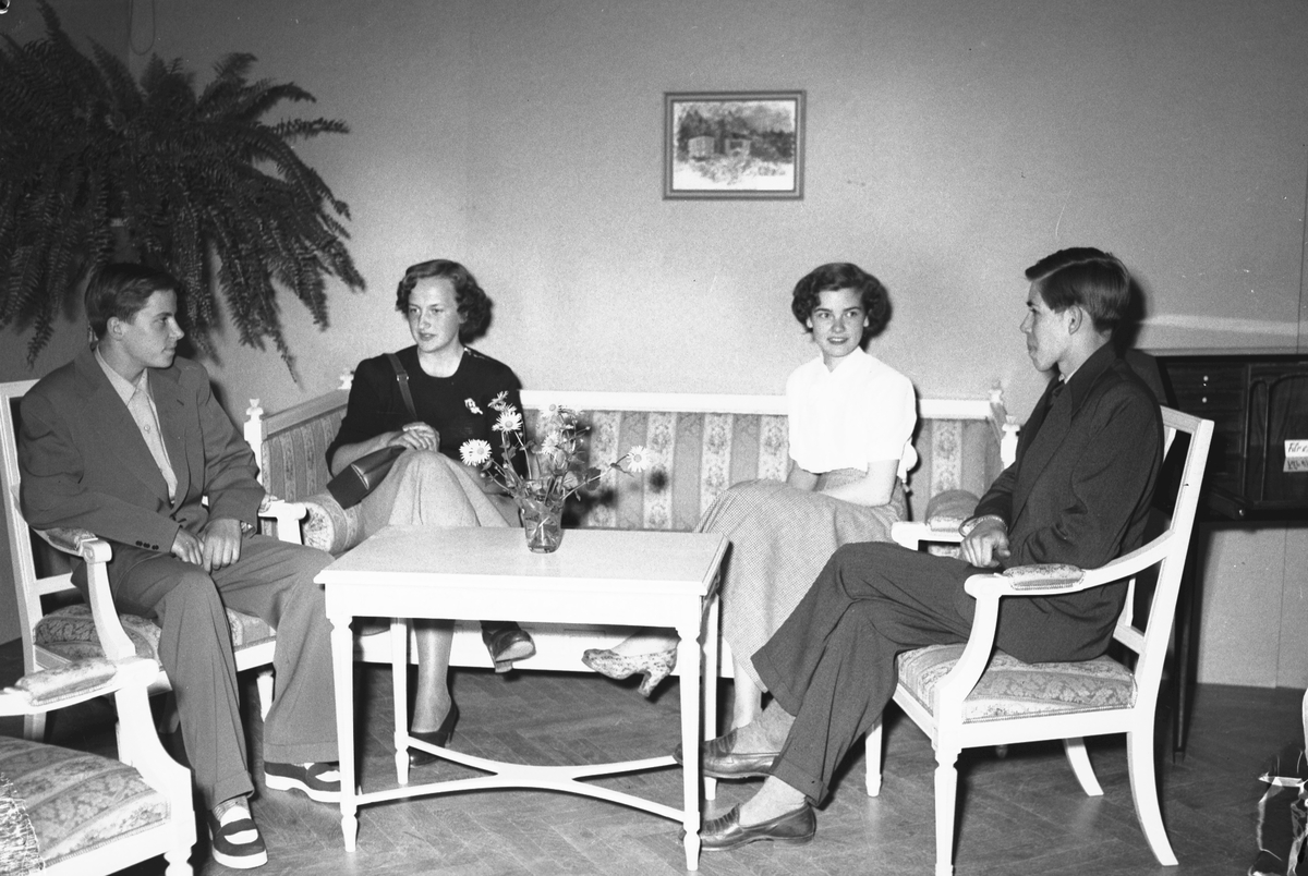 Yrkesskolornas avslutning på Stadshuset. Den 20 maj 1950. Damfrisörskeeleverna Margareta Nilsson och Ingrid Vadstedt provsitter den soffa som kamraterna på möbelsnickeriet utfört. Till vänster sitter Hans Englöf och till höger Åke Sjöstedt.