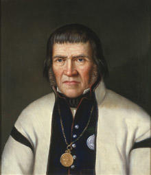 Portrett av Tallev O. Huvestad. Hvit trøye (jakke) og mørk vest kantet med rødt. Medalje hengende i kjede rundt halsen. (Foto/Photo)