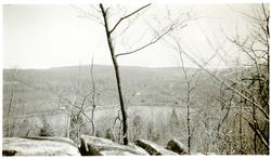 Motivet viser et vann med skogkledde åser rundt. Det ligger 
