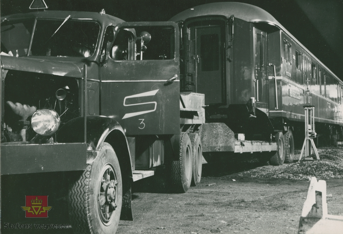 Sundsten's lastebil  med "S" på døra, og maskintilhenger.  Spesialtransport med drift på alle seks hjul, forflytter en konduktør og reisegodsvogn type DF37  21305 tilhørende NSB. I og med bildet er tatt i 1954, kan bildet stamme fra leveransen av vogna da den ble levert og satt i drift i 1955.