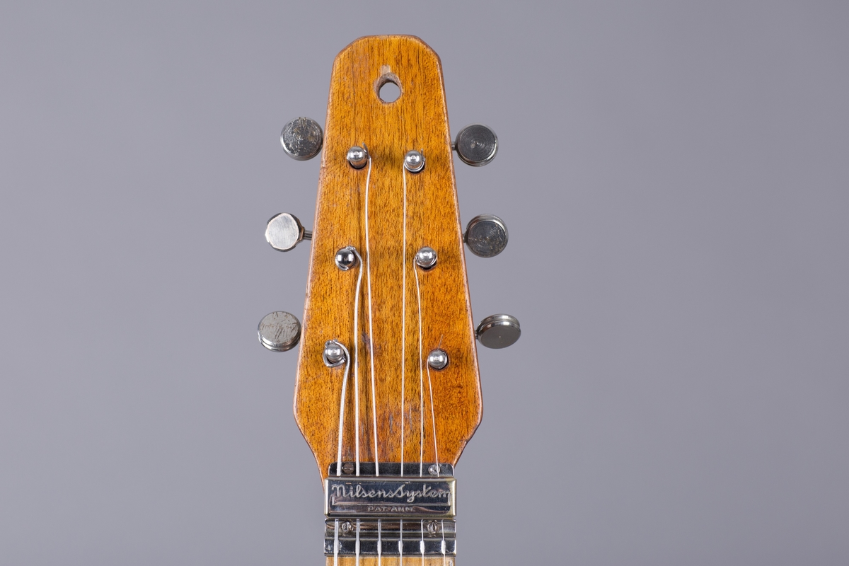 Elektrisk gitar med kropp og hals av mahogny. Magnet ved halsfeste og pickup ved strengefeste (NilsensSystem). Kontrollere for tilpasning og klangfarge. Tilpasning tilsvarer volum og gir størst volum på nivå 1. Enkelte av stemmeskruene er ikke originale.