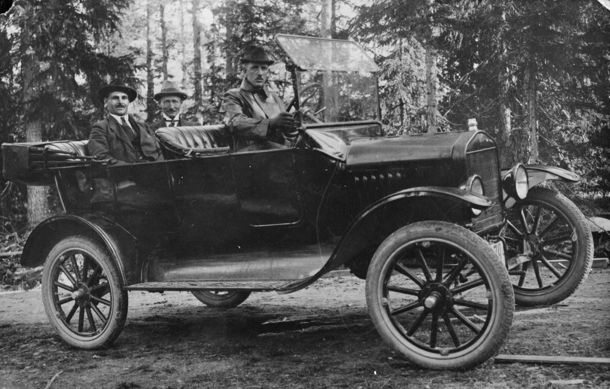 Tre män i en äldre bilmodell.