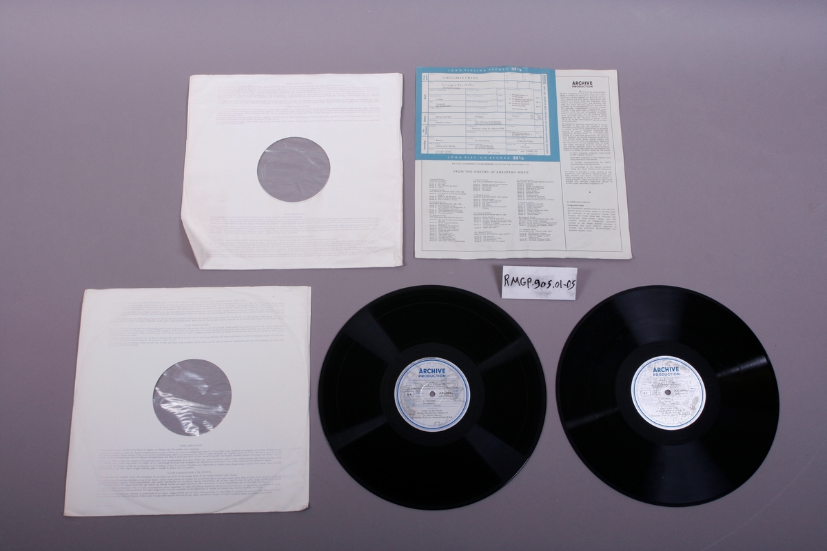 To grammofonplater i svart vinyl. Platene ligger i papirlommer med plastfôr. I tillegg et ark med tekst på begge sider.