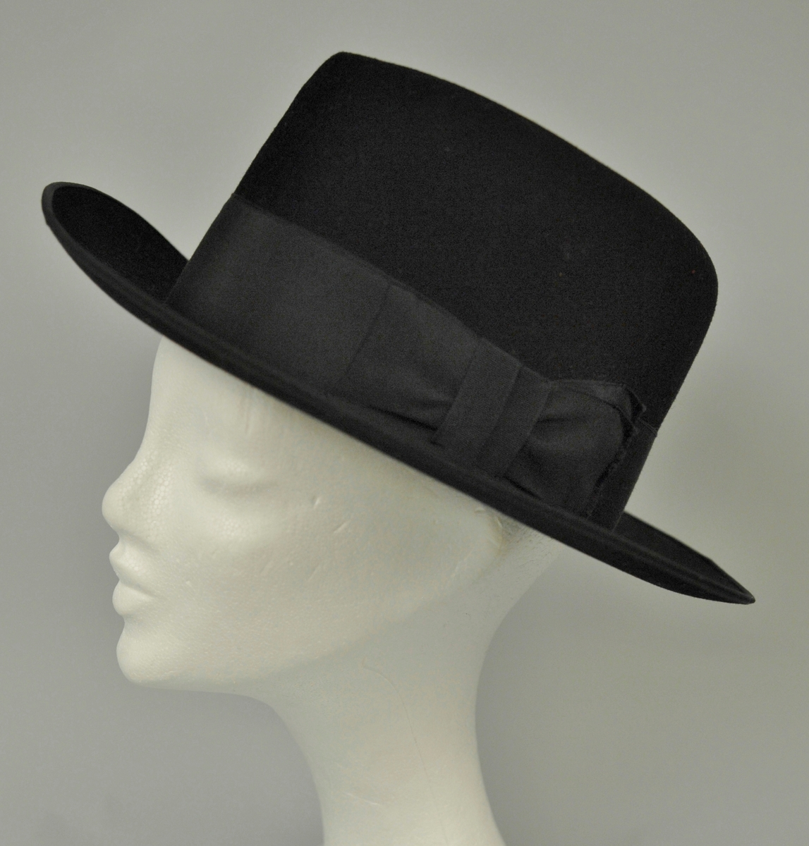 Hatten har høy pull. Bredt sort ripsbånd rundt pullen. Lyst brunt skinn i svettebrem innvendig. Lite brukt. "Penhatt". 