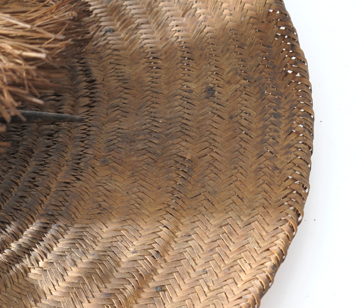 Vidbremmet hatt i mykt strå, brunt, med en liten sylindrisk  pull med  en 4,5 cm lang krans av strå rundt toppen. I toppen en sort  buet  fjær, gjennom pullen en hattenål i form av en fjærstilk.