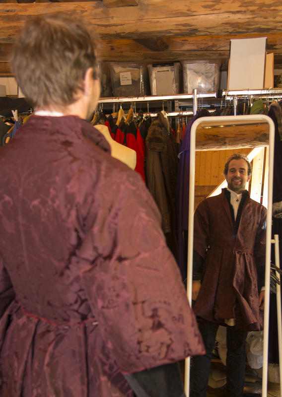 Mann i burgunderrød brokadejakke med store skjørt ser på seg selv i speilet og smiler. (Foto/Photo)