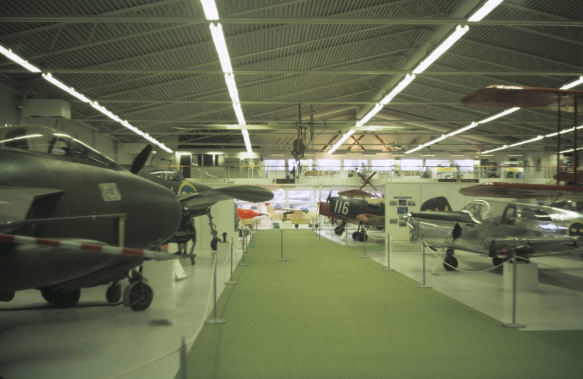 Interiör av Flygvapenmuseum, våren 1988. Mittgång och utställda flygplan längs sidorna.