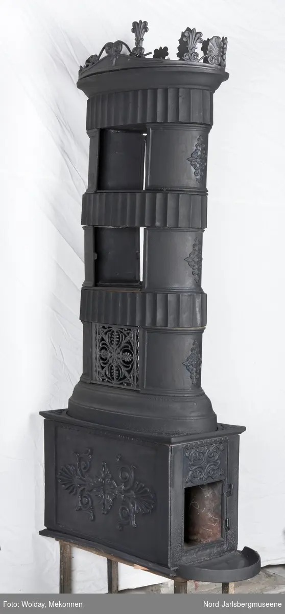 Ornamentikken som er tegnet i katalogen fra 1850, avviker noe fra ovnseksemplaret i museet. Røykkamrene på ovnen har rosettrelieff også på buet kortside, og palmettornamentet på fyrommets langside samt toppkransen avviker litt  på detaljnivå. Tverrkamrene i røyketasjene har store vertikale rifler (se anitkkens søyler).  Ovnen mangler dør, over døråpning et firedelt rokailleornament i flatt relieff.Toppkrans med palmetter og rokokkosnurrer.