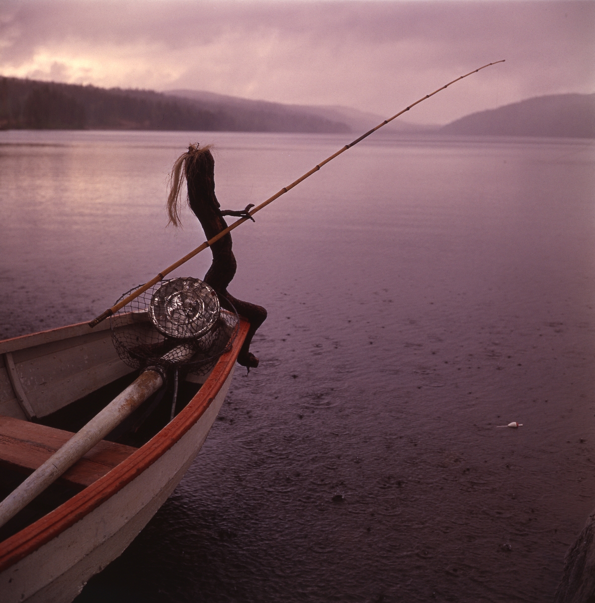 Trätrollet Skrälla Skrälle sitter i en roddbåt ute på sjön Ängratörn och metar. Det regnar.
