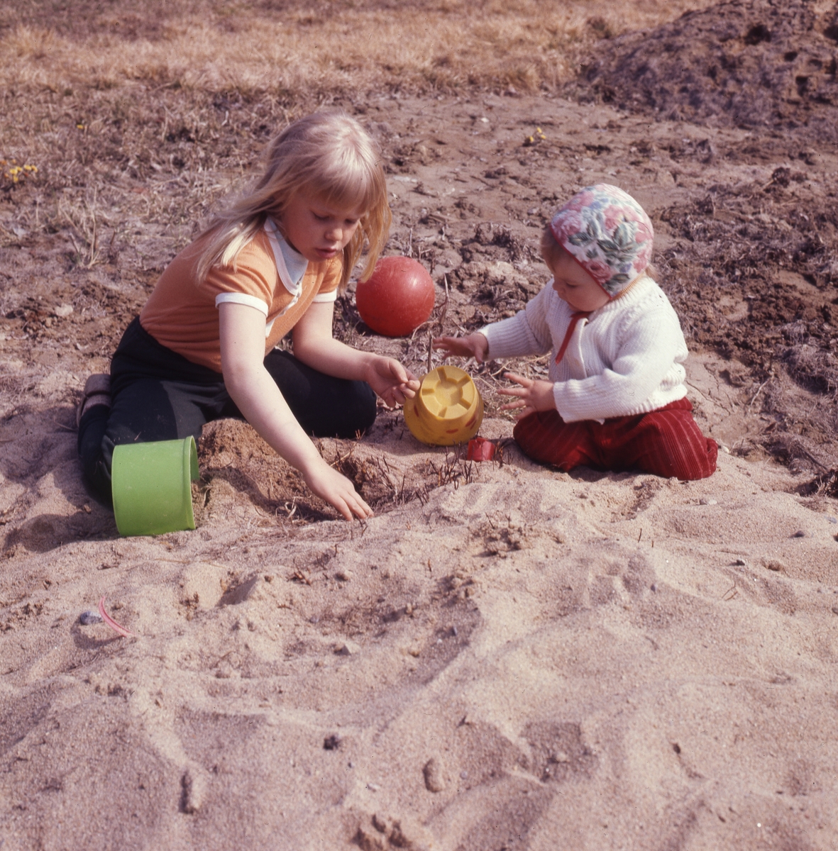 Sommarlek. Två barn sitter och leker i en sandhög.