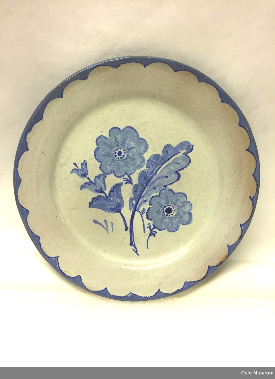 A: Mugge, B-C: 2 boller og D-K: 8 tallerkener i hvit- og blåglasert keramikk med dekor. L: Mugge