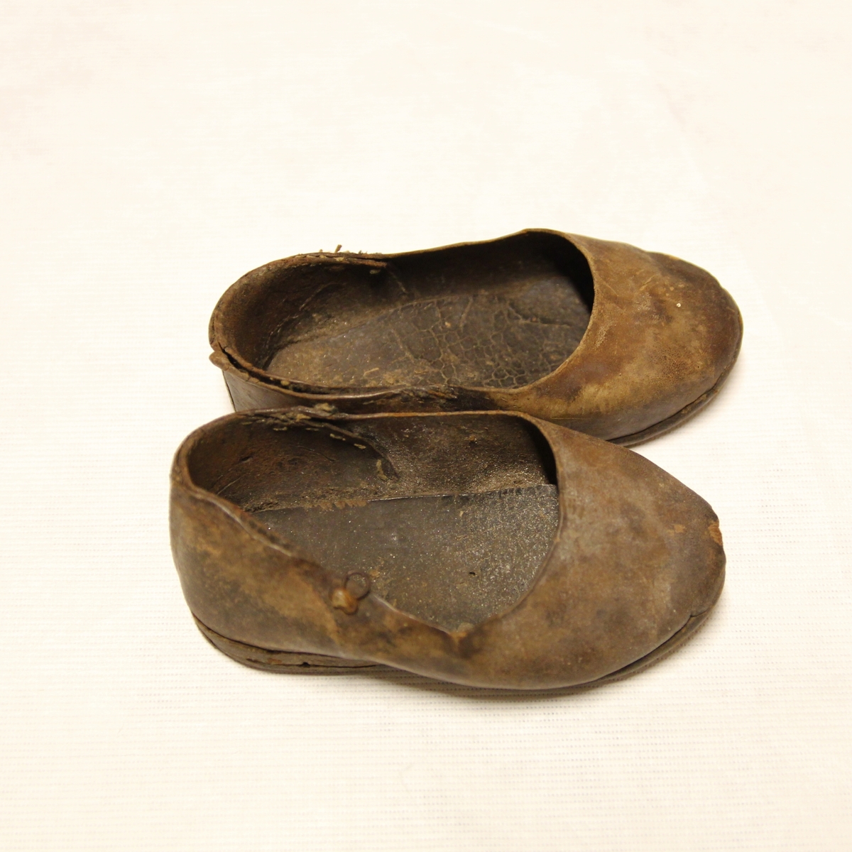 Et par små pikesko. Heimlagede av skinn med trenagler. Det har vært reimer på skoene. Meget slitt.