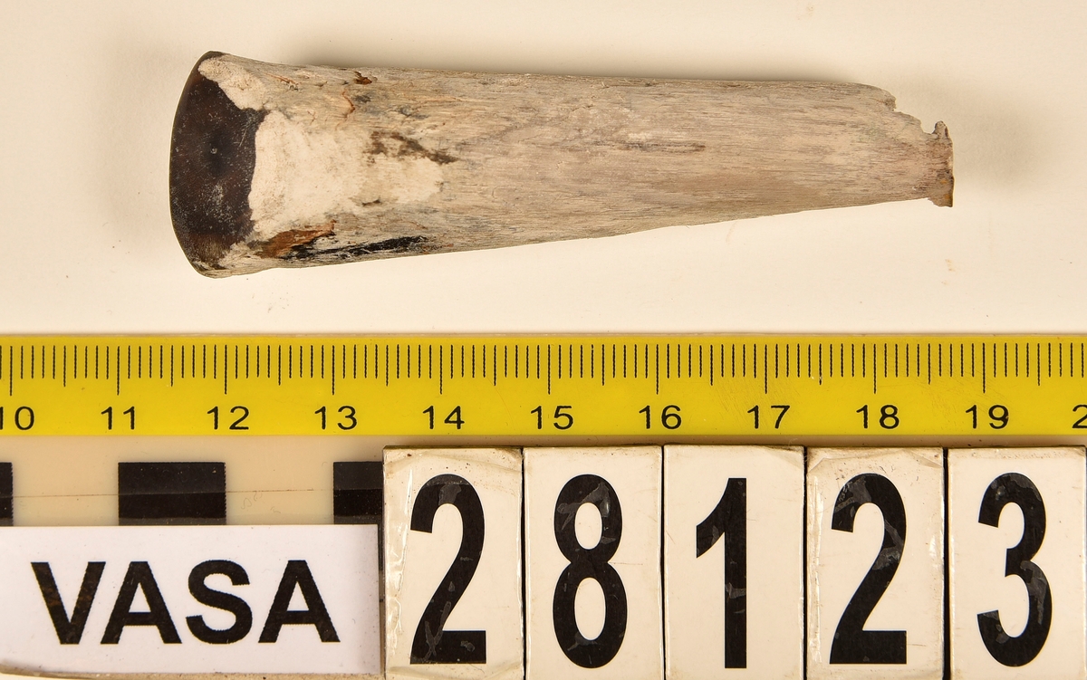 Fragment av horn. Avbruten i ena änden och sågad diagonalt till en spets i den andra änden. Ena sågytan har slipad sida. Hornets ursprungliga yta är bortnött och ytan känns närmast som torkat trä.