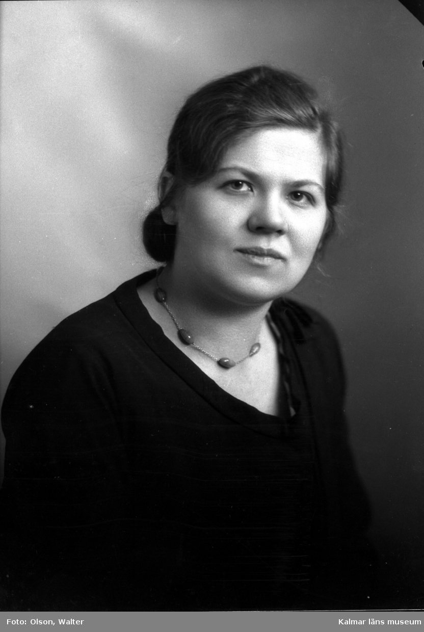 Ateljébild på en kvinna med håruppsättning, halsband och jumper. Enligt Walter Olsons journal är bilden beställd av fröken Ida Pettersson.