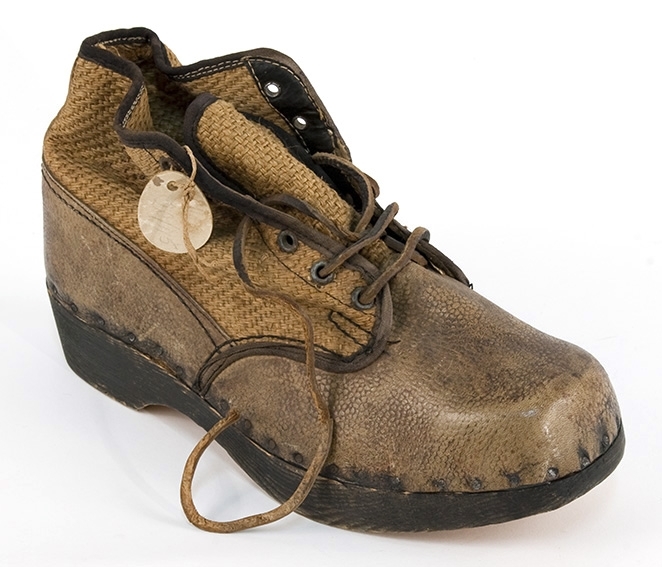 En høy, brun sko, eller lav støvel, med tresåle, lisselukking og overdel av strie (vrist, ankel) lær (hæl, tupp, side nederst. Antatt krigsprodukt.