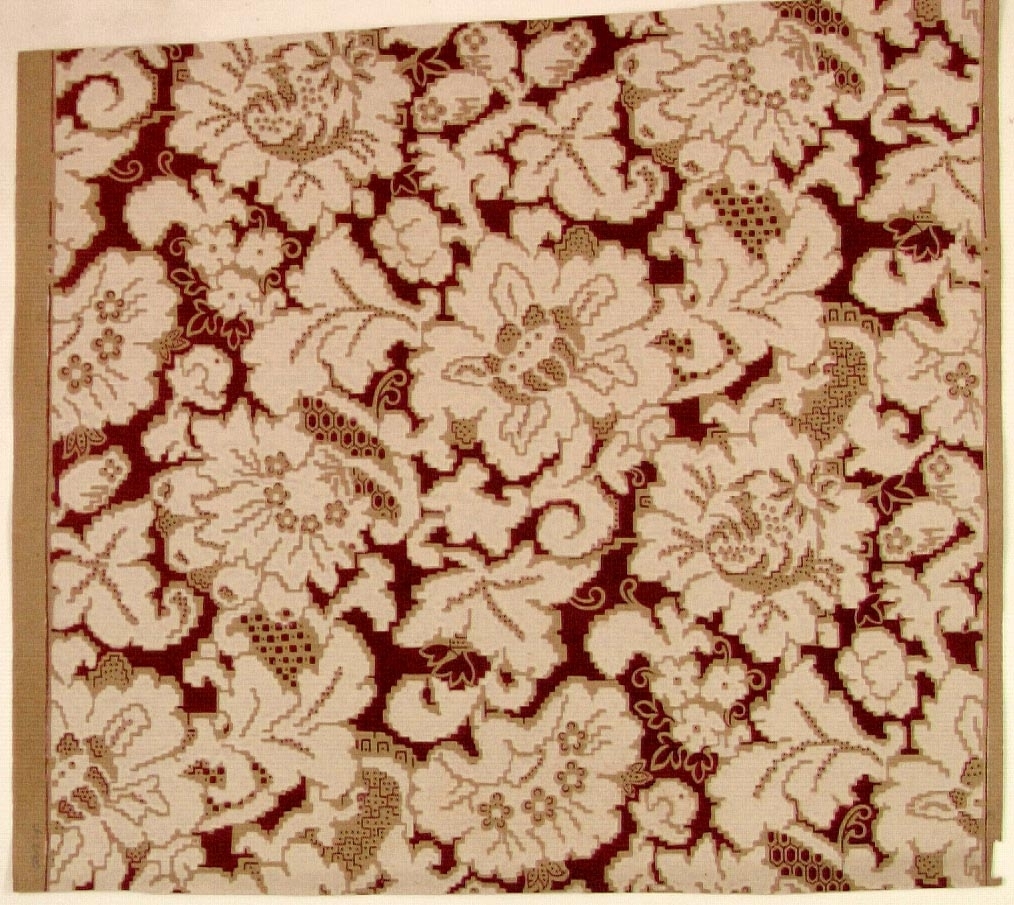 Ett ytfyllande silhuett-/blommönster i cremevitt och vinrött på ett beige genomfärgat papper. Bakgrunden delvis försedd med prickmönster.