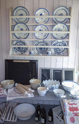 Tallerkenhyle som viser dype og flate tallerkener i hvitt porselen med blå blomsterdekor, kjøkkenhåndklær, boller, kjevler og tavler til å skrive på. (Foto/Photo)