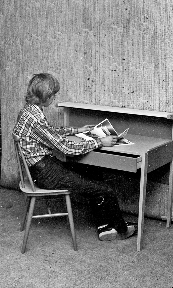 Ung mann som sitter ved pulten og leser et interiørmagasin.