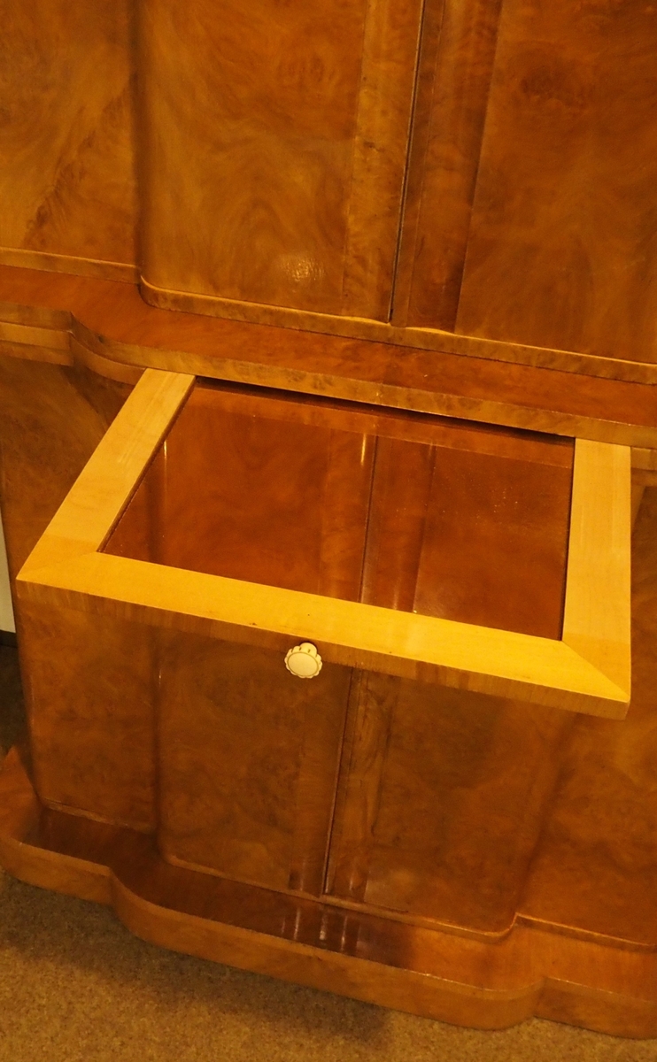 Cockailskap i to høyder med fire dører. Profilert korpus, sokkel, gurtlist og topplist. Mahogny med valnøttfiner; de øvre dørene er finert med lyst satintre på innsiden. Nedre skap har en hylle og en skuff festet øverst. Gurtlisten har en uttrekkbar hylle med ferskenfarget speilglass. Øvre del av korpus har dører som åpner til skap med belysning. Veggen bak, bunnen og to hyller er dekket med ferskenfarget speilglass. Øverst på veggen bak ses geometrisk dekor flankert av bladranker. På hver av dørenes innsider en hylle og gjennomhullet feste for cocktailpinner. Ti originale glasspinner med svaner er bevart.