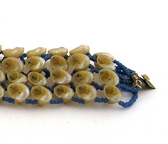 Armband av fyra rader små snäckor, och på de sammanbindande trådarna, små blå glaspärlor. Trasigt.
Bildar par med 34572:1.