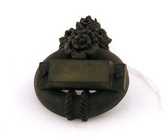 Brosch av bakelit i form av en kraftig ring med ett "påskruvat" tvärstycke. Undertill en blombukett. Nål av mässing.