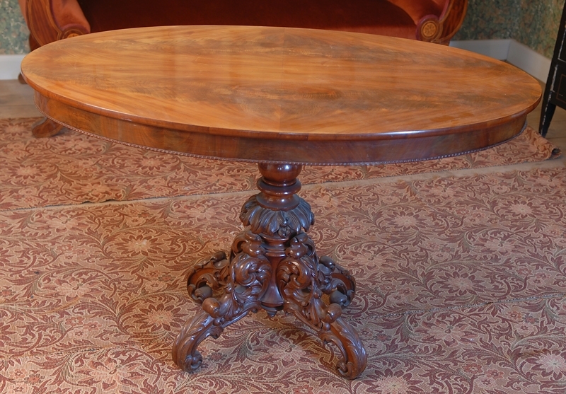Ovalt bord i mahogny. Skivan uppbäres av rikt svarvad pelare med 4 st fötter, som pryds av rocailleliknande sniderier.