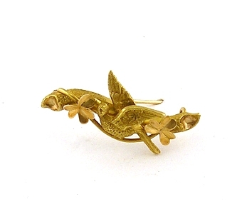 Brosch av guld som använts som schalnål till schal inv. nr. 87503. Motiv av fågel och treklöver.