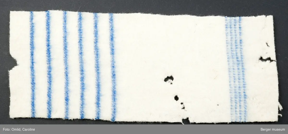 Hvitt teppe med blå striper i to felt; et med tette striper, ett med bredere stripere med større mellomrom