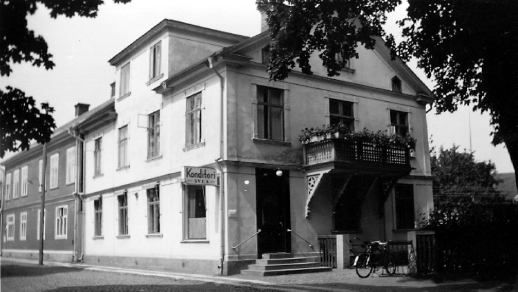 "I detta hus, Kyrkogatan 2, Hjo, föddes Yngve Sjöstedt den 3 aug. 1866. (Balkongen från senare tider). Bottenvåningen var delvis uthyrd till Skaraborgs Läns Enskilda Bank."