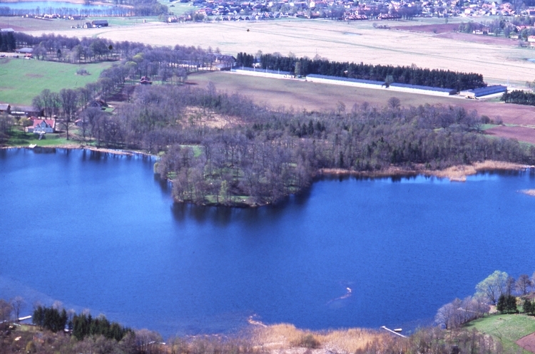 På udden i Husgärdessjön finns ruinerna efter Axevalla hus.
Fältet i bildens mitt är Axevalla hed.
Samhället i bakgrunden är Axvall.