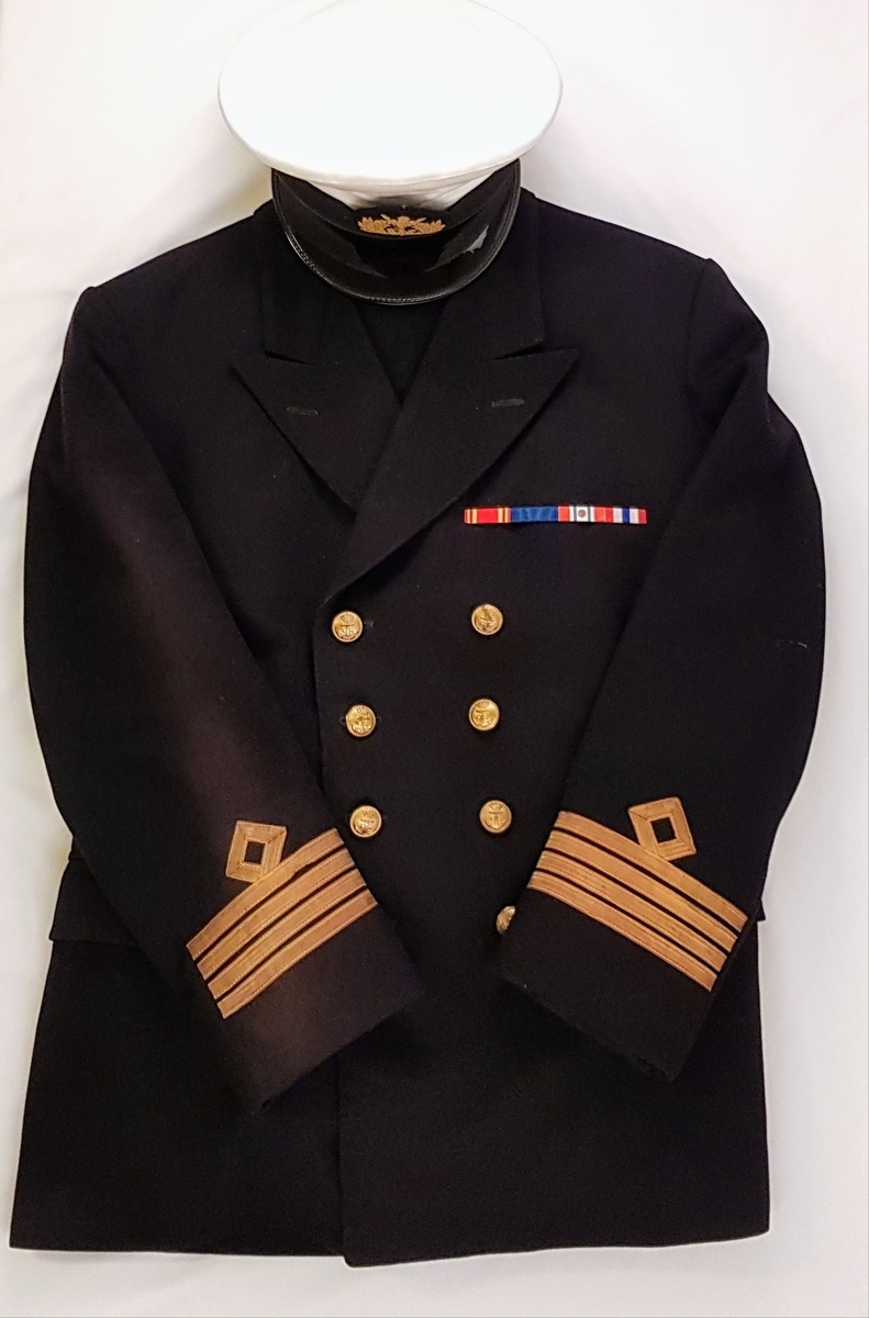 Norsk kapteinsuniformuniform bestående av bukse, jakke og lue i marineblått ullstoff. Jakken har tre gullstiper og diamant, noe som tilsier at dette er en kapteinsuniform.