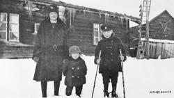 Personer, klær, ski og skistaver, bolighus.