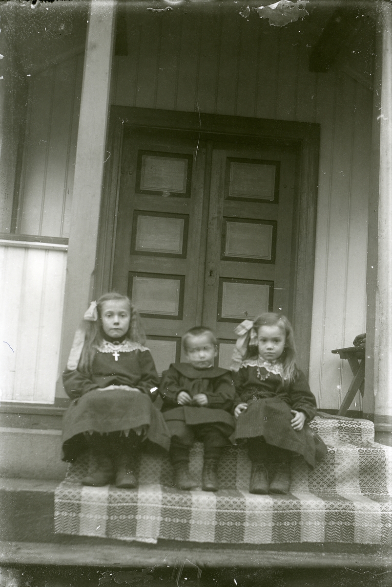 Tre barn sit på ei trapp.