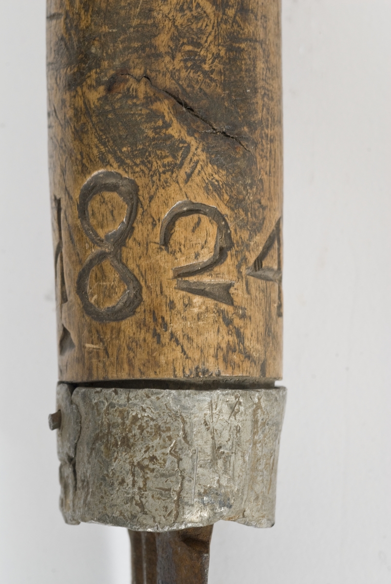 Tregrep med hvitt metall ring nederst. Knappen er formet i treverk..Grepet har innskåret intialer PISH 1824.
Rett tveegget klinge med elipseformet tverrsnitt. To midtstillt smale blodrender.Dekor for enden av blodrendene på begge sider.
