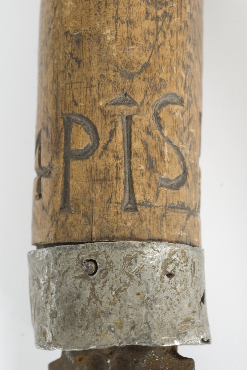 Tregrep med hvitt metall ring nederst. Knappen er formet i treverk..Grepet har innskåret intialer PISH 1824.
Rett tveegget klinge med elipseformet tverrsnitt. To midtstillt smale blodrender.Dekor for enden av blodrendene på begge sider.
