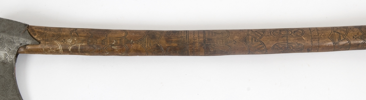 Asymmetrisk blad med lang øvre spiss og kortere nedre spiss.
Bladet er tynt, med påsmidd noe tykkere egg.
Øksehammeren har skaftehull og fliker.
Smedmerke formet som et skjell. Øksen har etset rankedekor på begge sider.
Skaftet er svakt krummet. Skaftet er merket på ryggen SON ANO 1700.Skaftet har skåret dekor i felter.