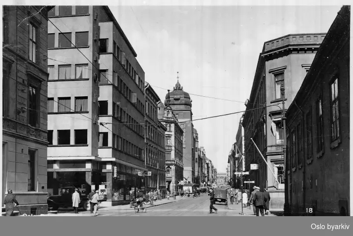 Prinsens gate opp mot krysset Store Strandgate som skiftet navn til Fred. Olsens gate i 1934. Paleet til høyre i bildet. Fred Olsen & co sitt hovedkontor til venste i bildet. Tårnbygningen er Hovedpostkontoret. Biler, spaserende. Postkort 18.