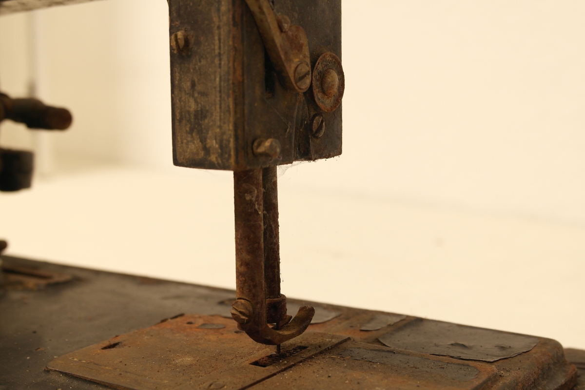 Symaskin i høvlet, pusset og beiset furu, samt støpt og malt jern. Maskinen står på ei treplate, som den opprinnelig kunne svinges opp fra. På maskinen er det fastskrudd en oval messingplate med fabrikkmerke.